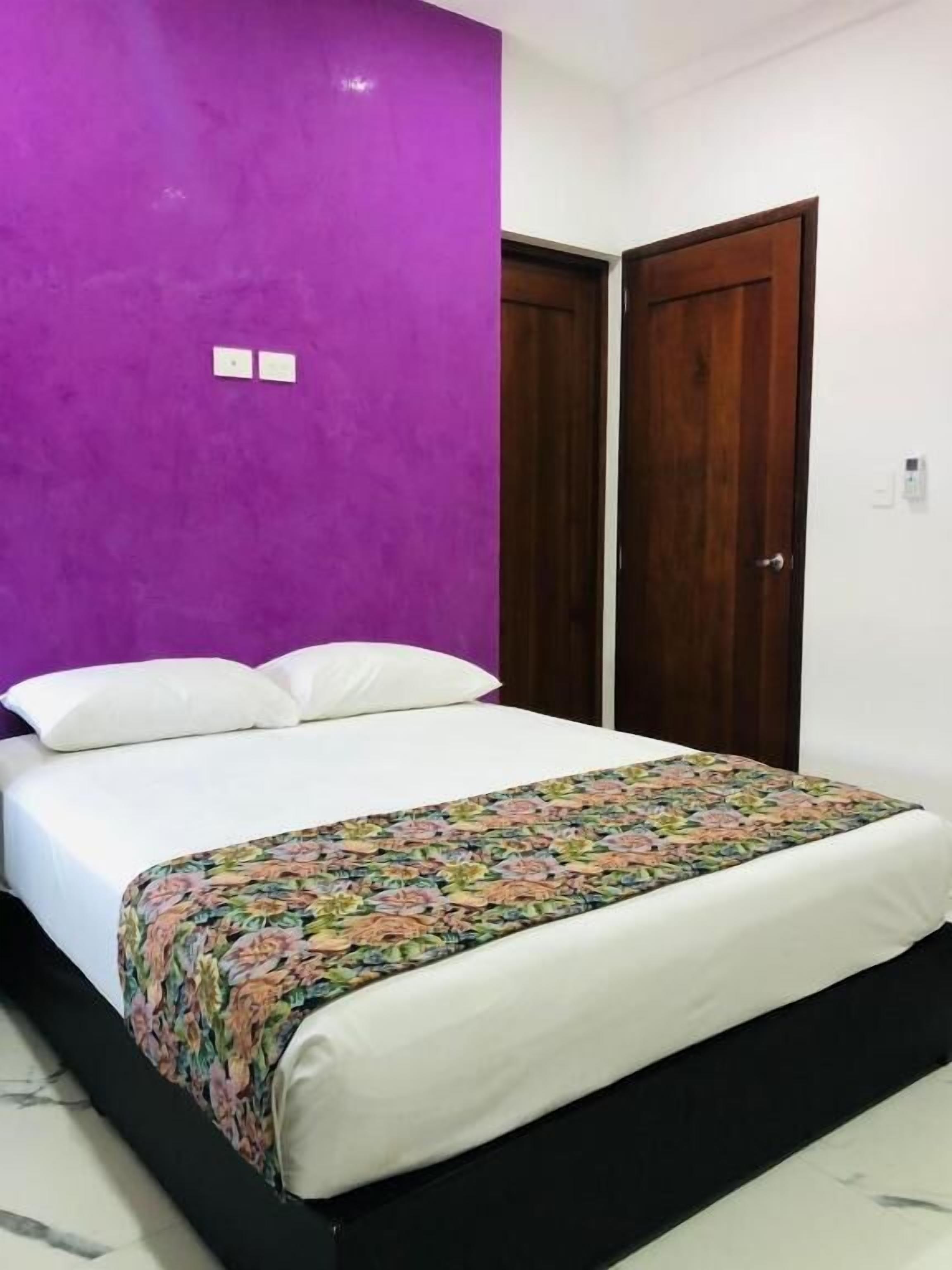 Un dormitorio con una cama, una pared morada y dos puertas de madera.