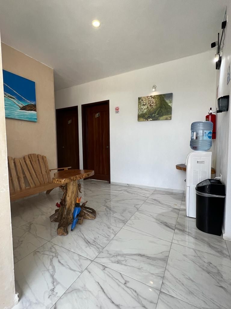 Una habitación con piso de mármol, una mesa de madera con diseño único, un dispensador de agua y un cesto de basura.