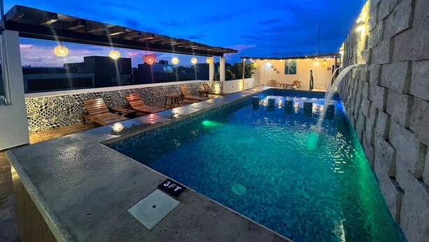 Una piscina en la azotea con sillones de descanso y una cascada.
