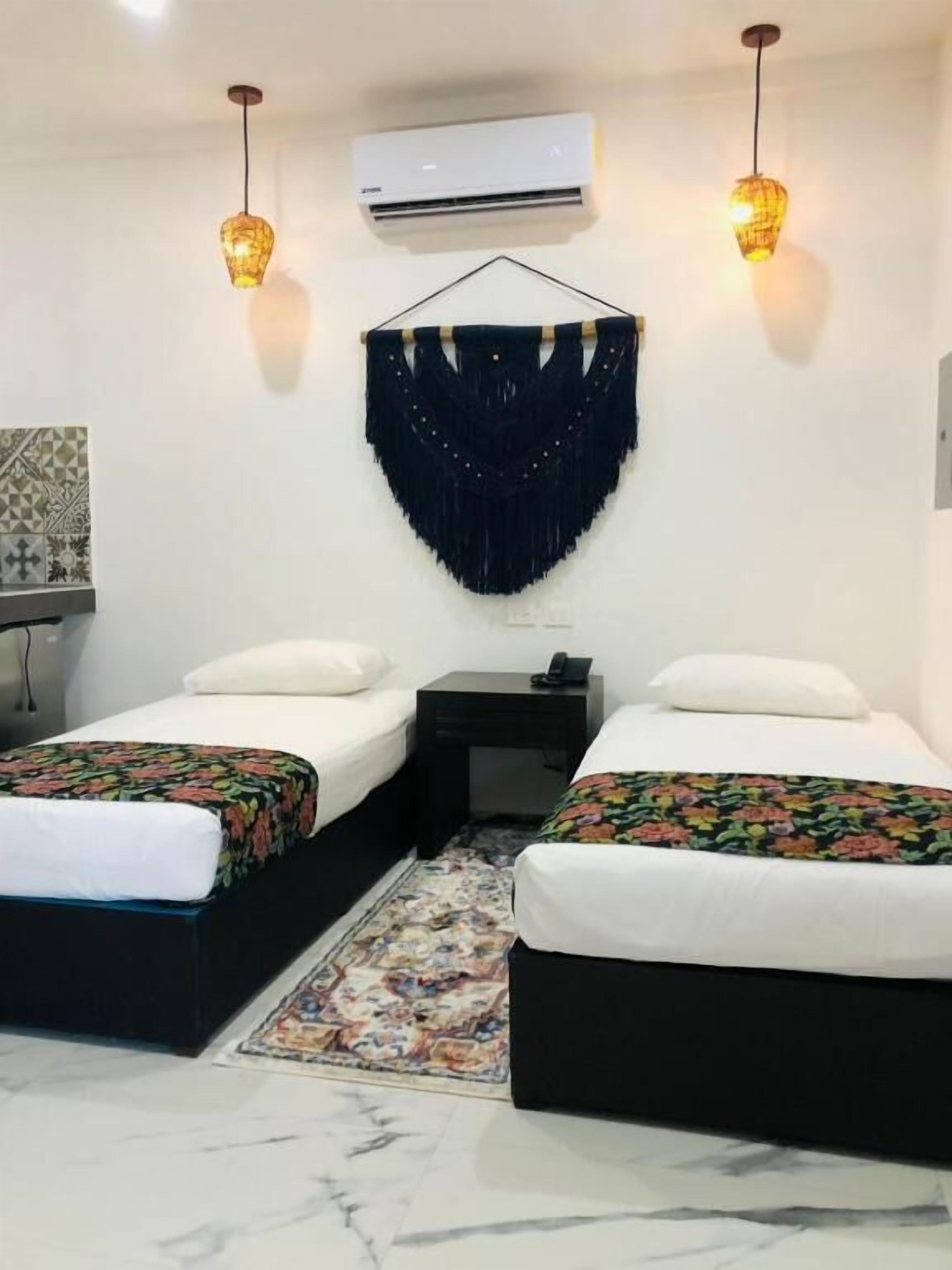 A hotel room with two beds, a decorative wall hanging, an air conditioner, and a small table with a phone.