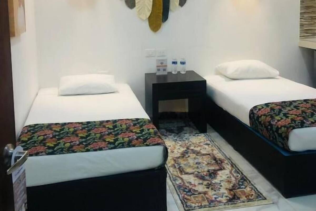 A hotel room with two beds, a small nightstand, an air conditioning unit, and a decorative wall hanging.