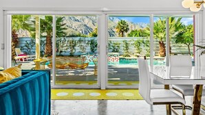 A modern living room with a large sliding glass door leading to a pool area, featuring a mountain view and outdoor furniture. - Birdcage Palm Springs - A Ryson Property (Palm Springs)