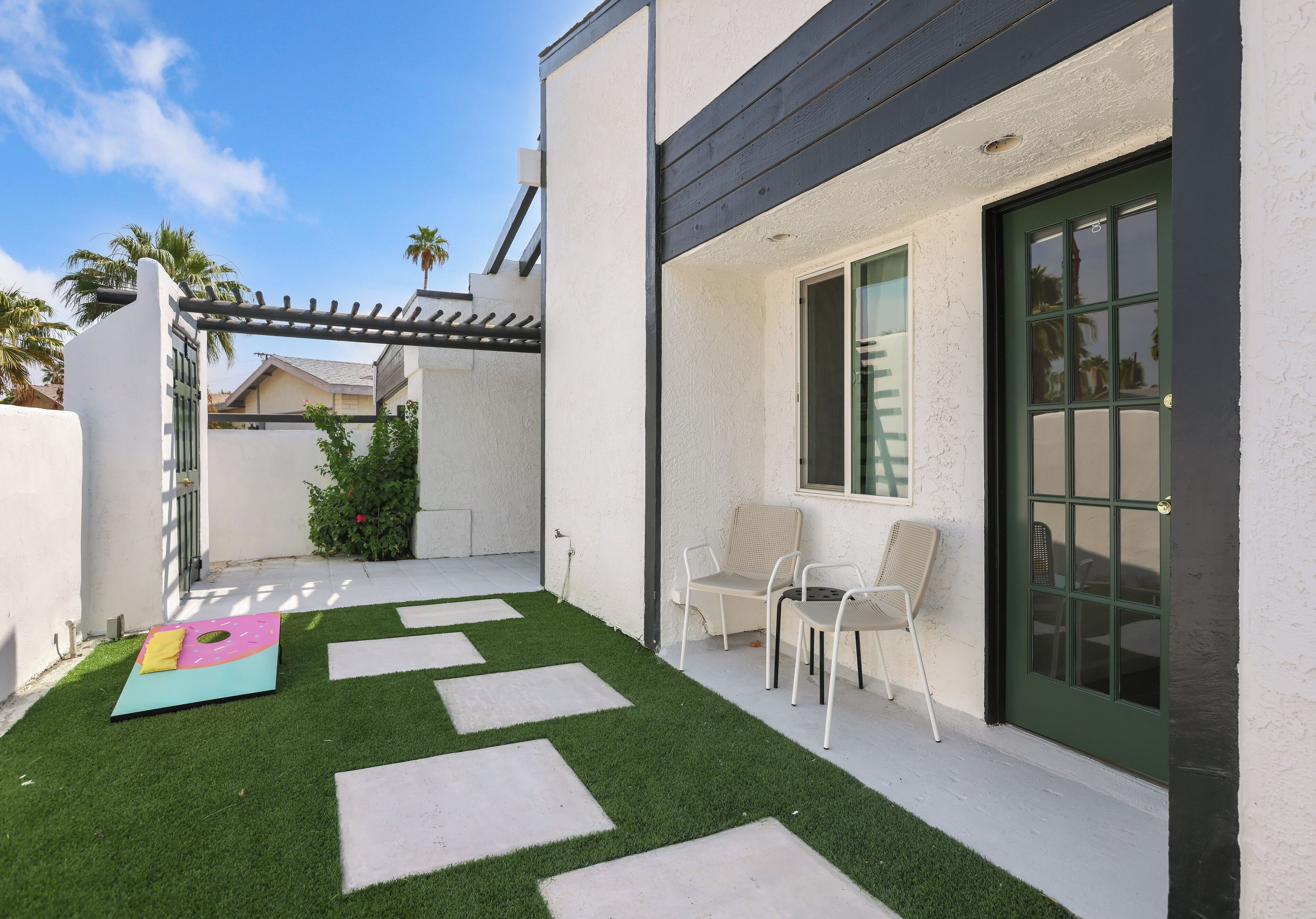 A modern patio with artificial grass, a pergola, and outdoor seating.
