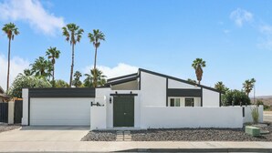 A modern single-story house with a white exterior, a green front door, and a garage door. - Desert Green Serenity - A Ryson Property (Palm Springs)