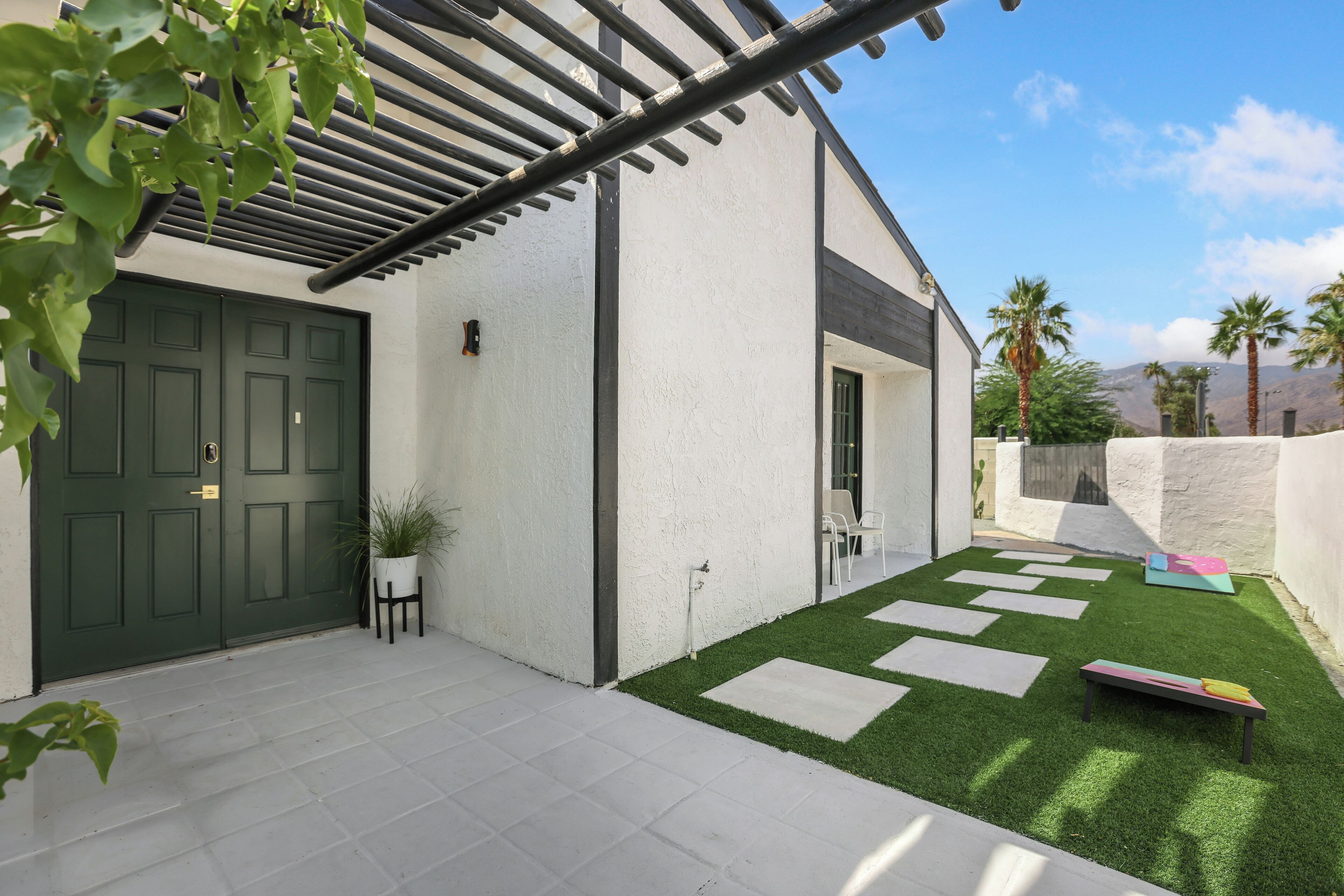 A modern house with a green door, white exterior walls, and a small patio with artificial grass and stepping stones.