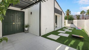 A modern house with a green door, white exterior walls, and a small patio with artificial grass and stepping stones. - Desert Green Serenity - A Ryson Property (Palm Springs)