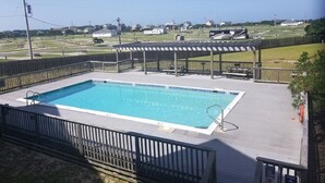 Una piscina rectangular con muelle de madera y escalera metálica, rodeada por una cerca de madera.