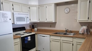 Una cocina con armarios blancos, microondas, estufa, lavavajillas y encimera de madera.