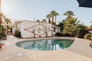 A swimming pool with a geometric mural, surrounded by palm trees and a building with a red roof. - Casa Coyote - A Ryson Property (Palm Springs)