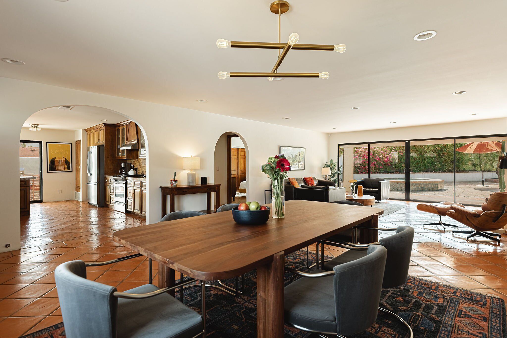 Un vaste espace dédié à la salle à manger, avec une table et des chaises en bois, un lustre moderne et une vue sur l’extérieur grâce à de grandes fenêtres.