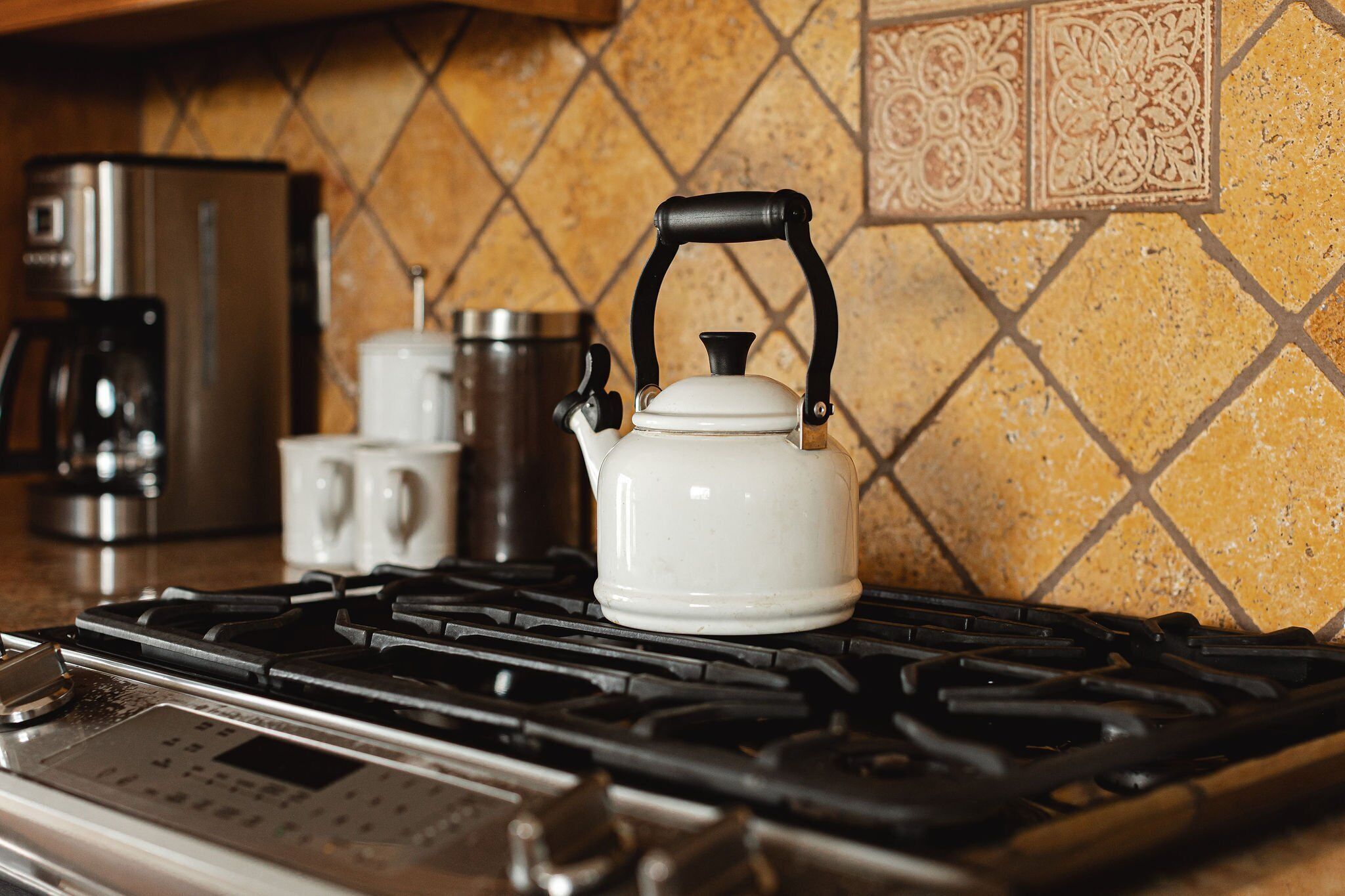A kitchen with a gas stove, a kettle, a coffee maker, and a microwave.