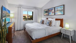 A hotel room with a large bed, a TV, a nightstand, and a window with curtains. - Convenient & Cozy Downtown - A Ryson Property (Palm Springs)