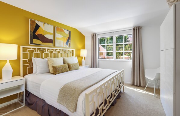 A bedroom with a bed, two bedside tables, a window with curtains, and a chair. - Chic Downtown Bungalow - A Ryson Property (Palm Springs)