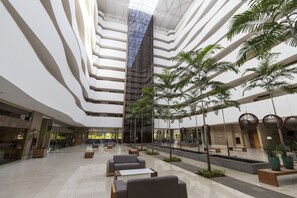 Un amplio atrium con asientos escalonados, una fuente central y palmeras de interior.