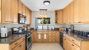 Une cuisine dotée de meubles en bois, de plans de travail en granit, d’une cuisinière et d’une fenêtre donnant sur un paysage verdoyant.