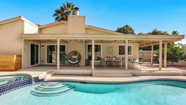 Un espace aménagé au bord de la piscine, avec un patio couvert, une piscine aux carreaux bleus et du mobilier d’extérieur.