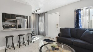 A modern kitchen with stainless steel appliances, a dark-colored sofa, and a glass coffee table. - Simple Elegance - A Ryson Property (Indio)
