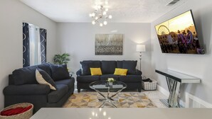 A modern living room with a sofa, coffee table, and a TV mounted on the wall. - Simple Elegance - A Ryson Property (Indio)