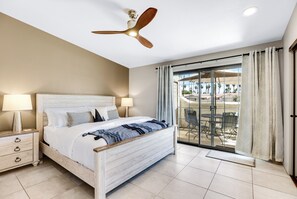 A bedroom with a bed, nightstands, a ceiling fan, and a view of an outdoor patio with chairs and a table. - Mountain Vistas Forever - A Ryson Property (Palm Springs)