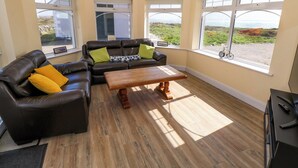 A living room with a brown leather sofa, a wooden coffee table, and large windows with a view of the sea. - Tí Tom Nárta (Teeranea)