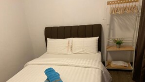 A neatly made bed with white bedding and two rolled blue towels.