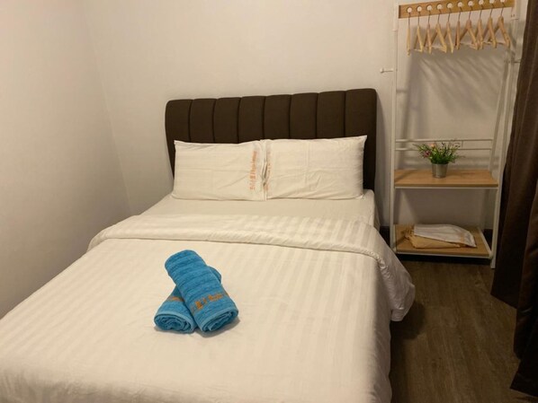 A neatly made bed with white bedding and two rolled blue towels.