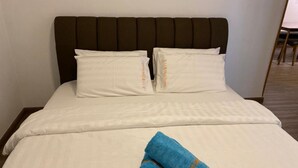 A bed with a dark headboard, white bedding, and two pillows with text on them. A blue towel is folded on the bed.
