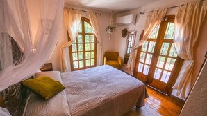 Un dormitorio con cama, una silla y ventanas amplias con cortinas.