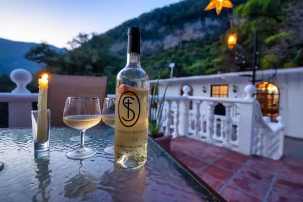 A bottle of wine, a glass, and a lit candle on a table with a view of a mountainous landscape.