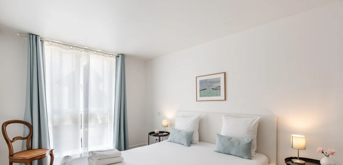 Una habitación de hotel con una cama, una silla, una mesita de noche, una lámpara y un cuadro en la pared.