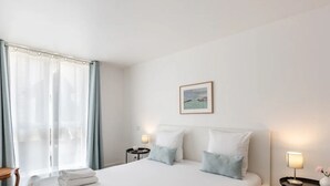 Quarto de hotel com cama, poltrona, mesa de cabeceira, abajur e um quadro na parede.