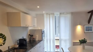 Cozinha moderna com armários brancos, bancada preta e área de refeições com mesa e cadeiras brancas.