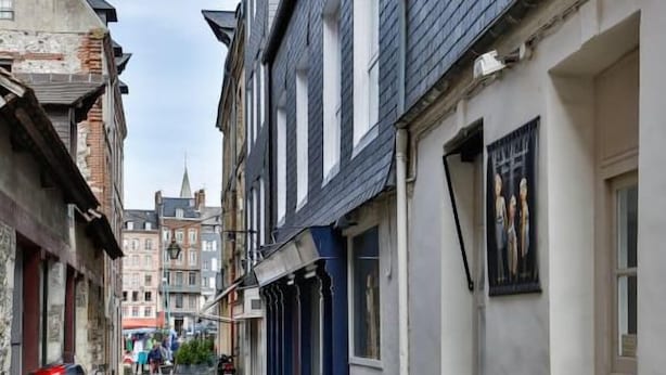Uma estreita rua de calçada, ladeada por edifícios históricos, alguns com sinais de desgaste e outros com fachadas modernas.