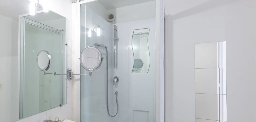 Une salle de bain moderne avec une douche à parois de verre, un miroir rond et un miroir rectangulaire.