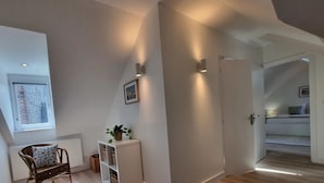 En modern inredning med ett sluttande tak, en inbyggd hylla med växter, en flätad stol och en vit dörr som leder till ett annat rum.
