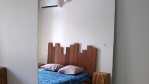 A bedroom with a wooden headboard, a bed with blue bedding, a small wooden stool, and a ceiling fan.