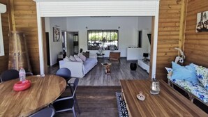 A spacious living area with a wooden ceiling, a large window, a sofa, a dining table, and a coffee table.