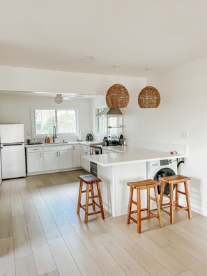 Eine moderne Küche mit weißen Schränken, einer großen Kochinsel mit Sitzgelegenheiten, einer integrierten Waschmaschine und einem Deckenventilator.