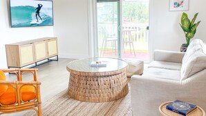 Ett modernt vardagsrum med en platt-TV, ett runt, flätat soffbord, en vit soffa och ett litet sidobord med en bok på.
