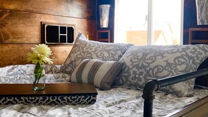 Ein Bett mit gemusterten Textilien, eine Vase mit Blumen und ein Nachttisch mit einer dekorativen Schachtel.
