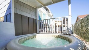 Ein Whirlpool im Freien mit einer Holzterrasse und einem weißen Geländer, umgeben von einer Hecke und einem Haus im Hintergrund.