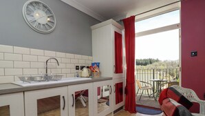 A compact kitchen with a sink, white cabinets, and a red curtain. - The Tack Room (Lydney)