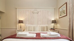 A hotel room with a large bed, two bedside tables, lamps, a framed picture on the wall, and a neatly made bed with folded towels. - The Tack Room (Lydney)