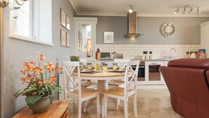 A modern kitchen with white cabinetry, a dining table with chairs, a red sofa, and a potted plant on the side table. - The Tack Room (Lydney)