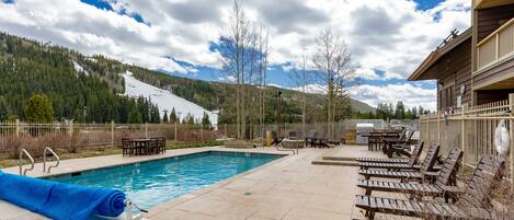 A pool area with lounge chairs, a covered pool, and a view of a mountainous landscape.