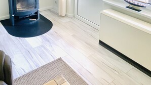Un salon moderne avec un poêle à bois noir, un radiateur blanc et une grande fenêtre donnant sur un paysage verdoyant.