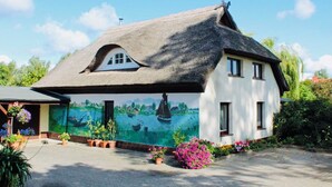 Une maison avec un toit de chaume et une fresque représentant une scène de navigation sur un de ses murs.