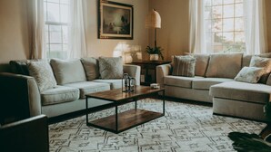 A living room with two sofas, a coffee table, a lamp, and a painting on the wall. - The Conestoga Cottage | Hot Tub, Rustic Charm, Near Downtown Lancaster (Conestoga)