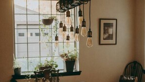 A dining area with a wooden table and chairs, hanging light fixtures, and potted plants by a window. - The Conestoga Cottage | Hot Tub, Rustic Charm, Near Downtown Lancaster (Conestoga)