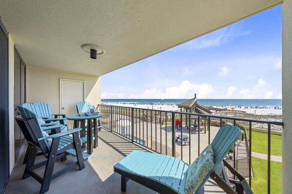 A balcony with chairs and a table, overlooking a beach with a fence and people. - Phoenix II 2012 (Orange Beach)